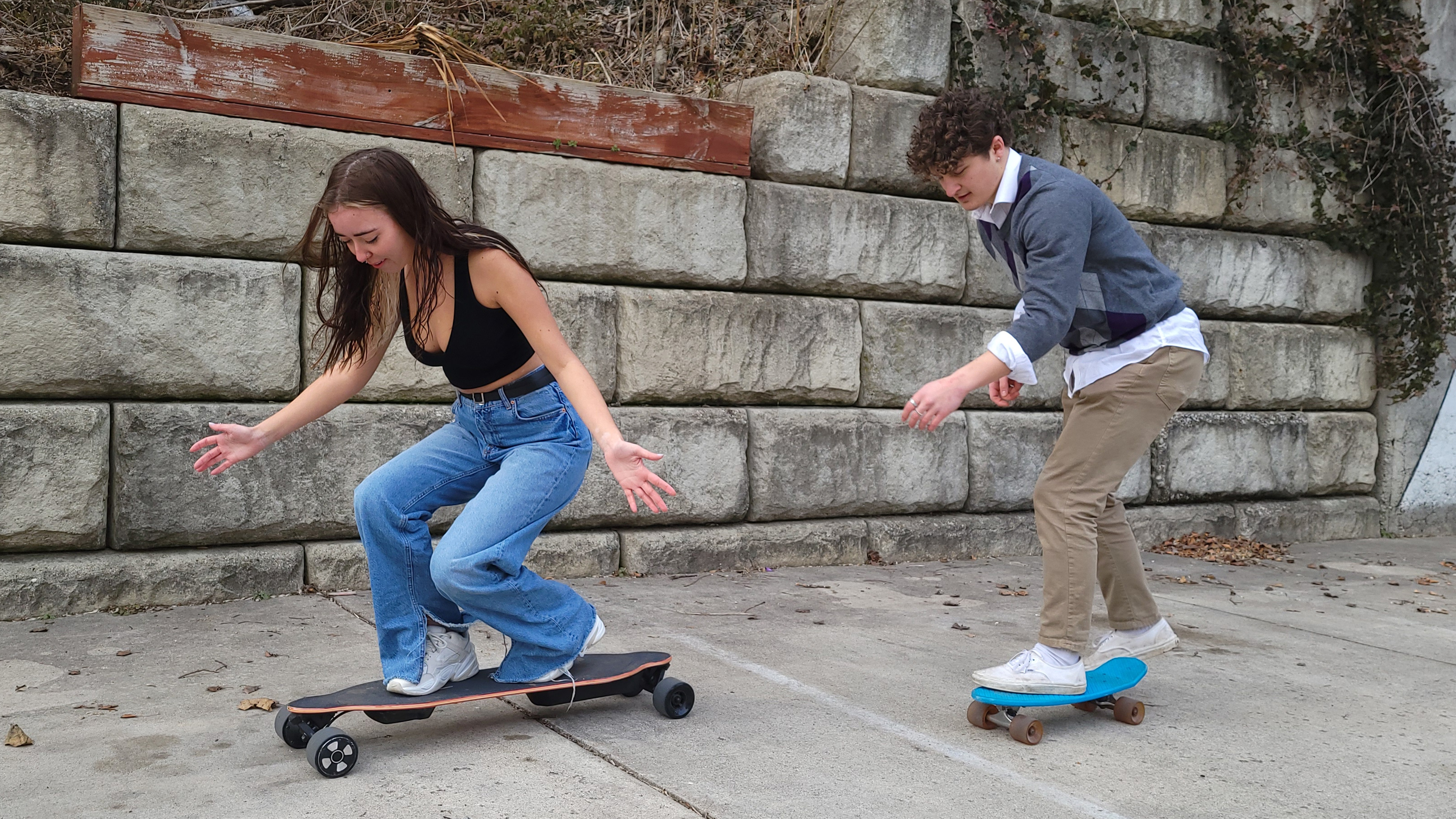 Two People Riding JEDENO Sprinter Electric Skateboards next to Grey Brick Wall