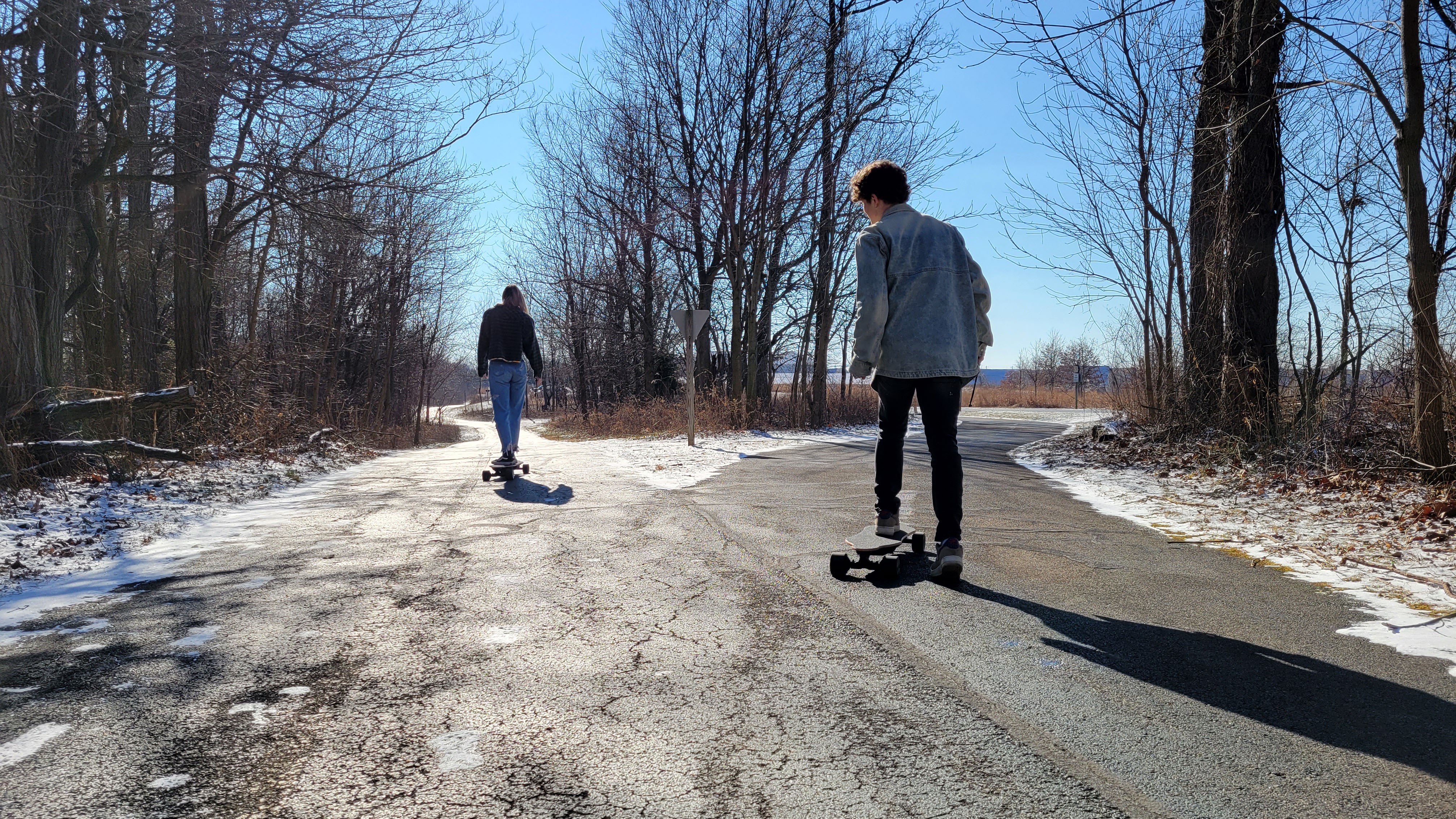Two People riding JEDENO Sprinter Electric Skateboards on Path with Fork looking away